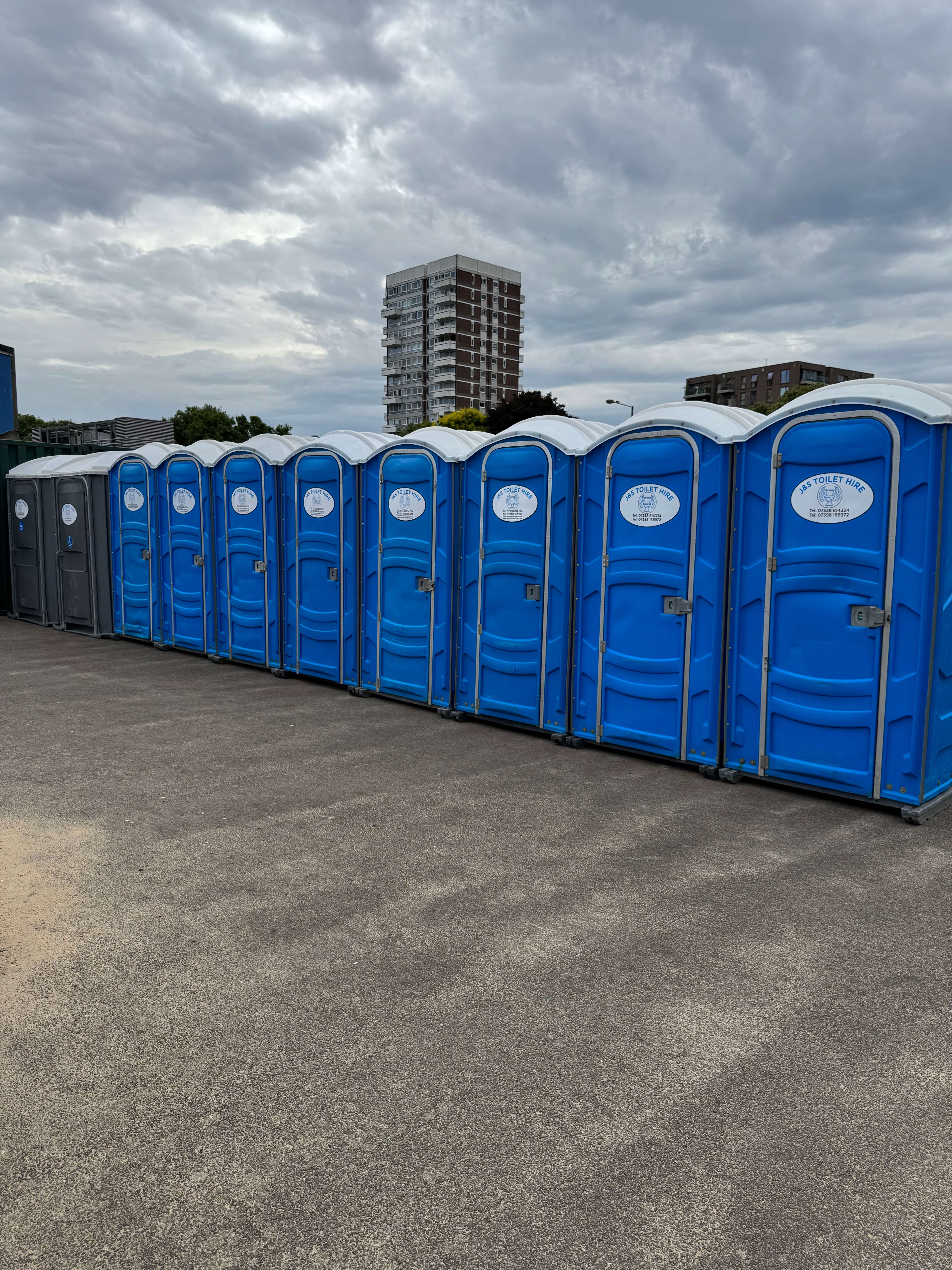 Long line of blue portable toilets on concrete for large-scale event with apartment buildings in background