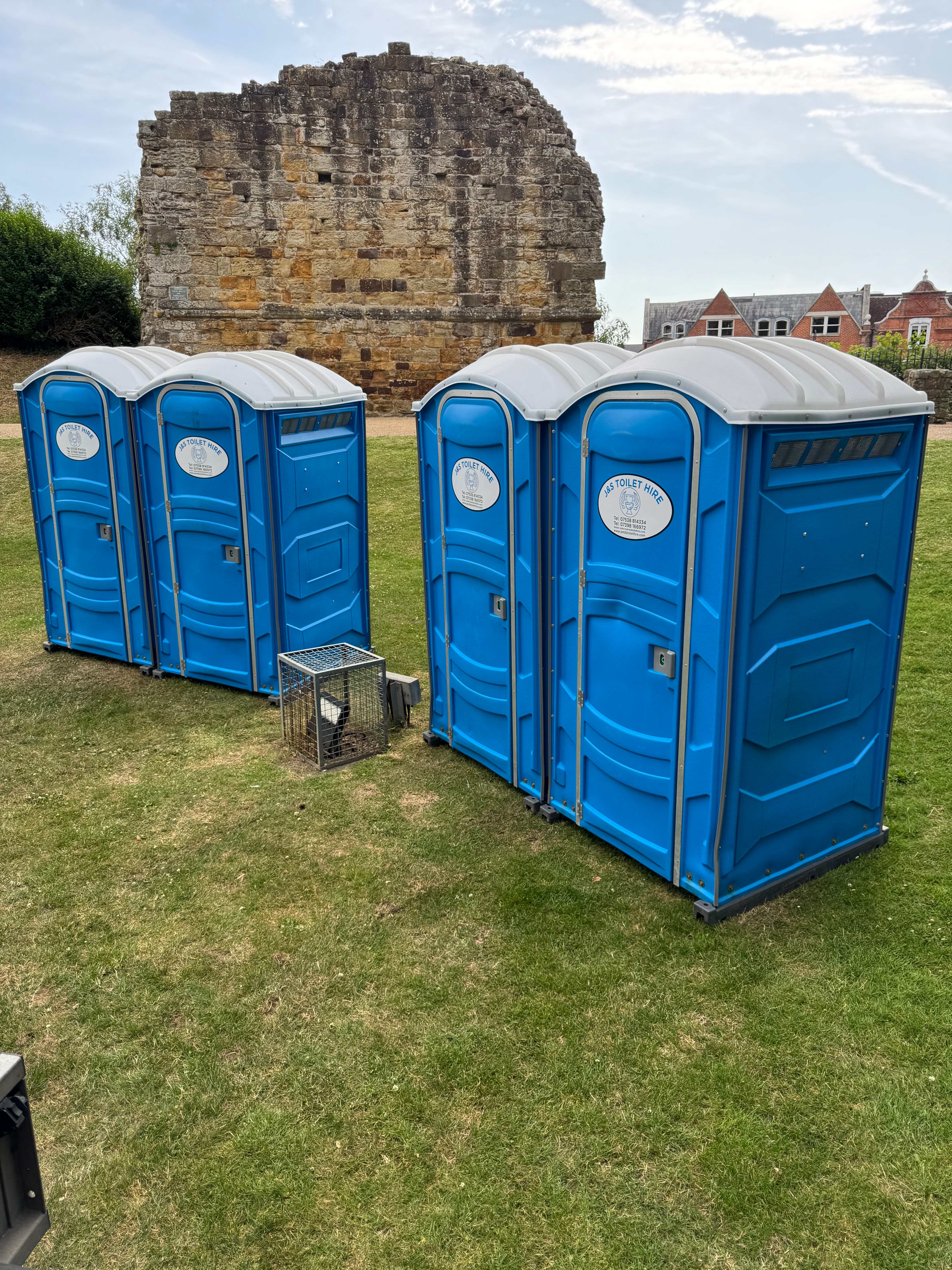 Event portable toilets positioned on grass near historic stone castle ruins