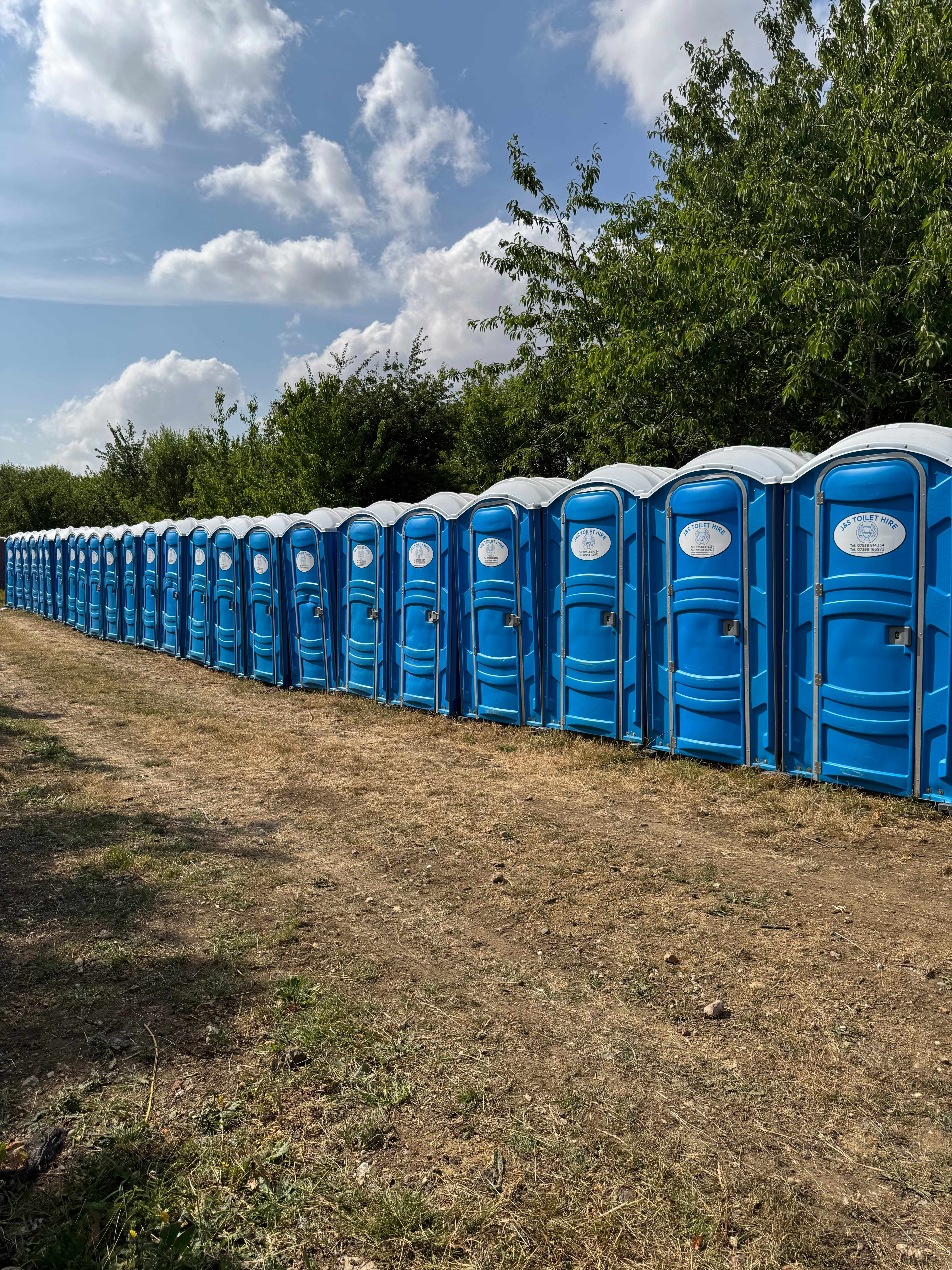 Very long row of many blue portable toilets in field demonstrating large capacity for major events